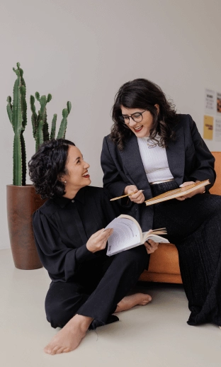 Duda e Marina sentadas olhando uma para a outra e sorrindo.
